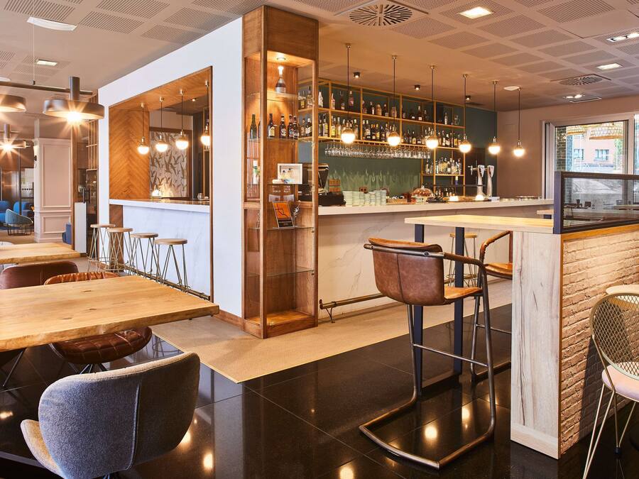 A modern bar area with wooden and metal furniture, a bar counter, and a view of the street outside.