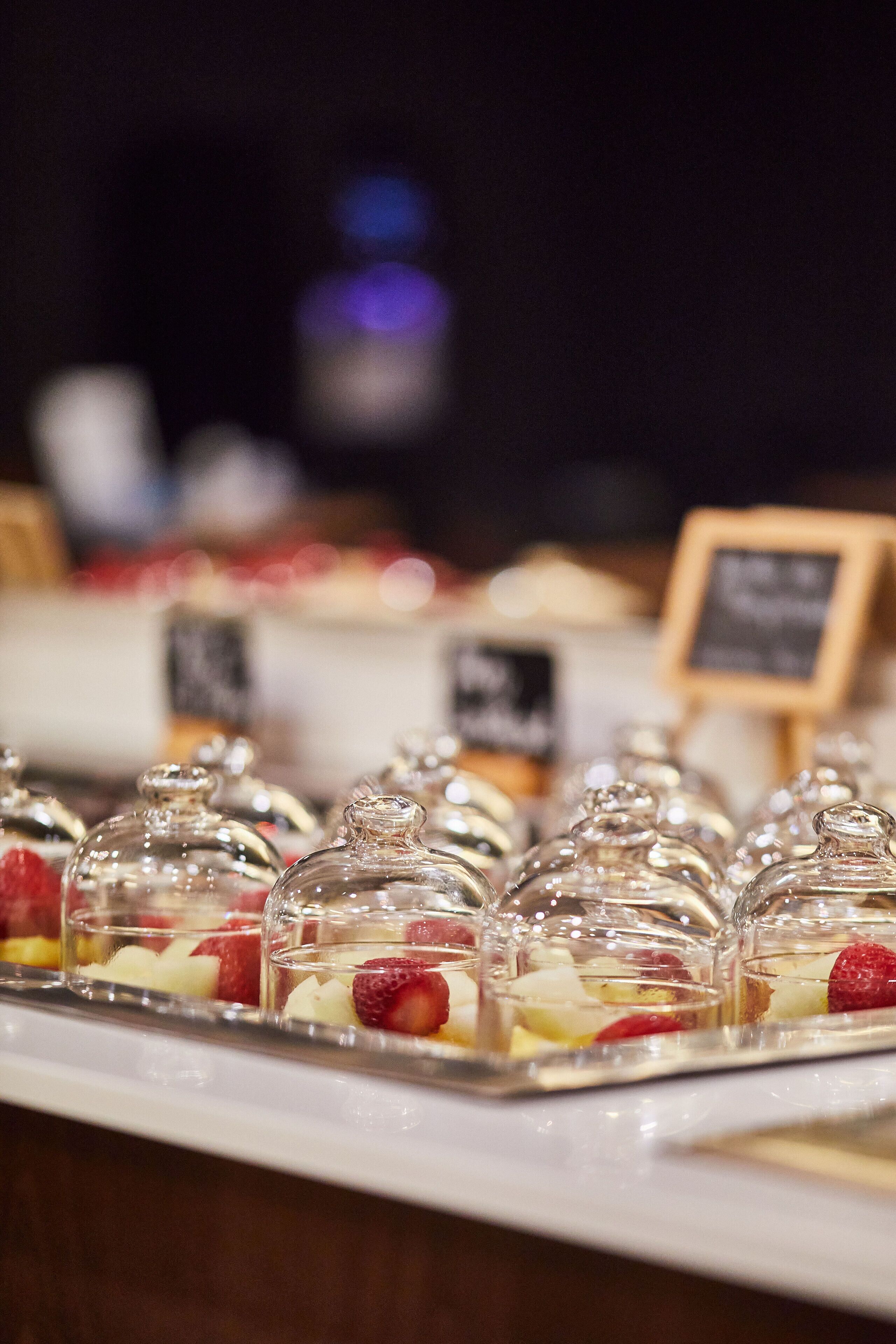 A dessert display with clear glass domes containing fruit and a chalkboard sign in the background.