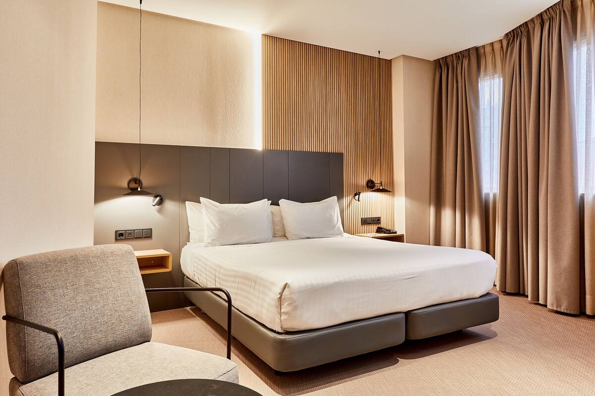Ein modernes Hotelzimmer mit einem großen Bett, einem Sessel und einem Nachttisch.