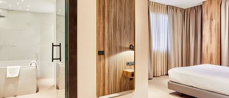 A modern hotel room with a large bed, a wooden panel wall, a bathroom with a bathtub, and a mirror.