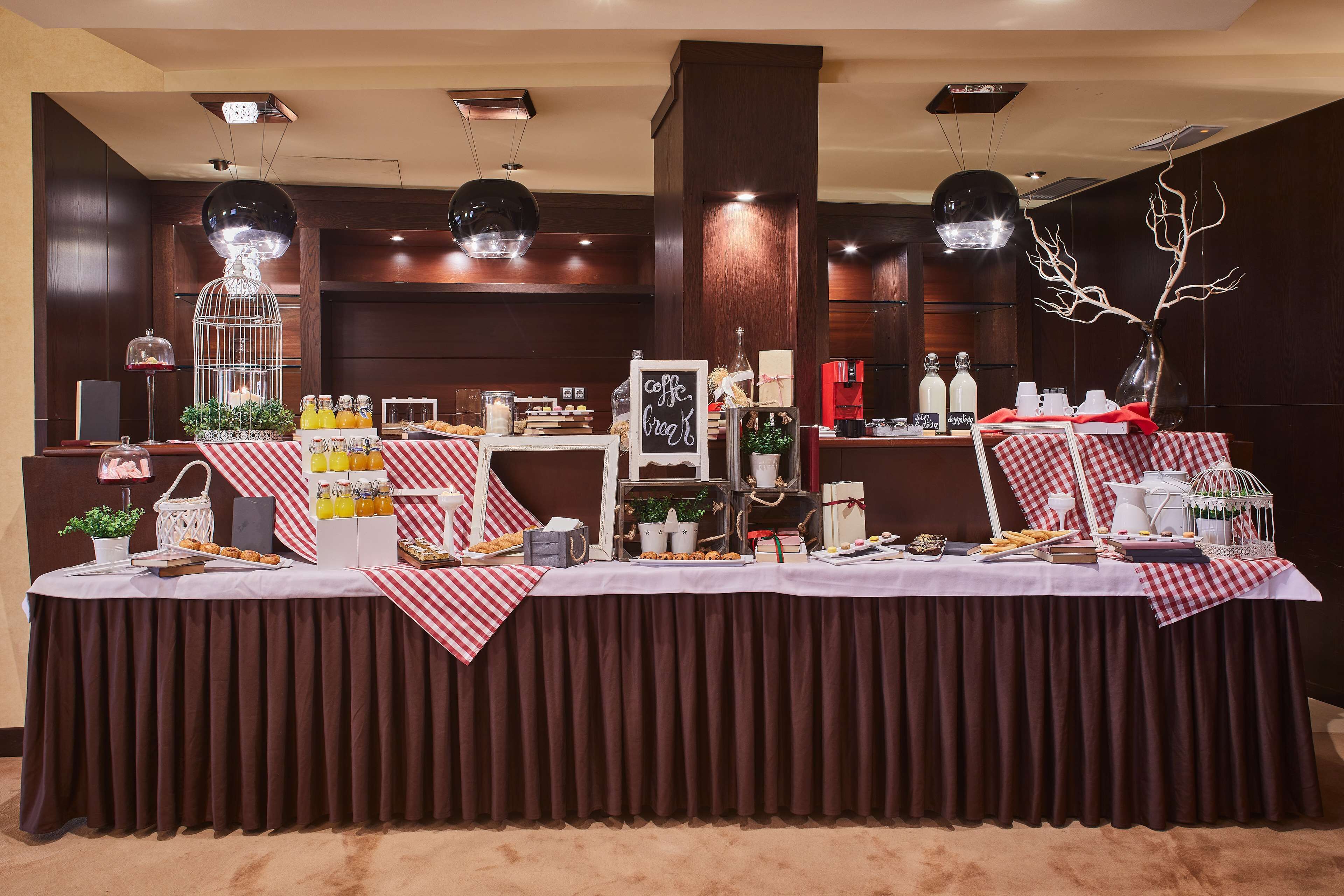 Disposição de buffet com diversos alimentos e bebidas, uma árvore decorativa e uma placa indicando café e croissants.