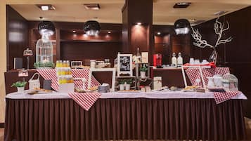 Montaje tipo bufé con diversos alimentos y bebidas, un árbol decorativo y un cartel que indica café y croissants.