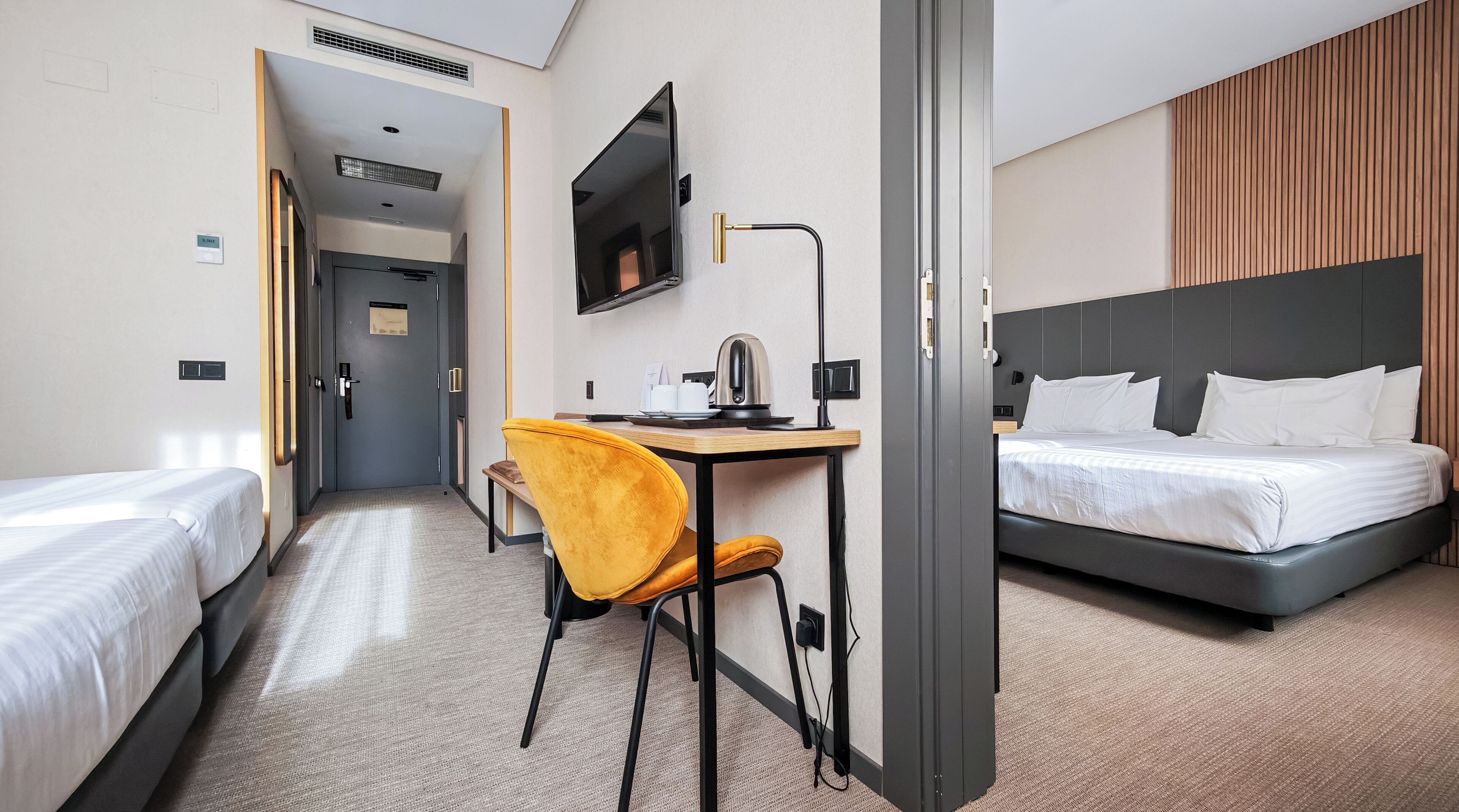 A hotel room with two single beds, a desk with a chair, a TV, and a kettle.