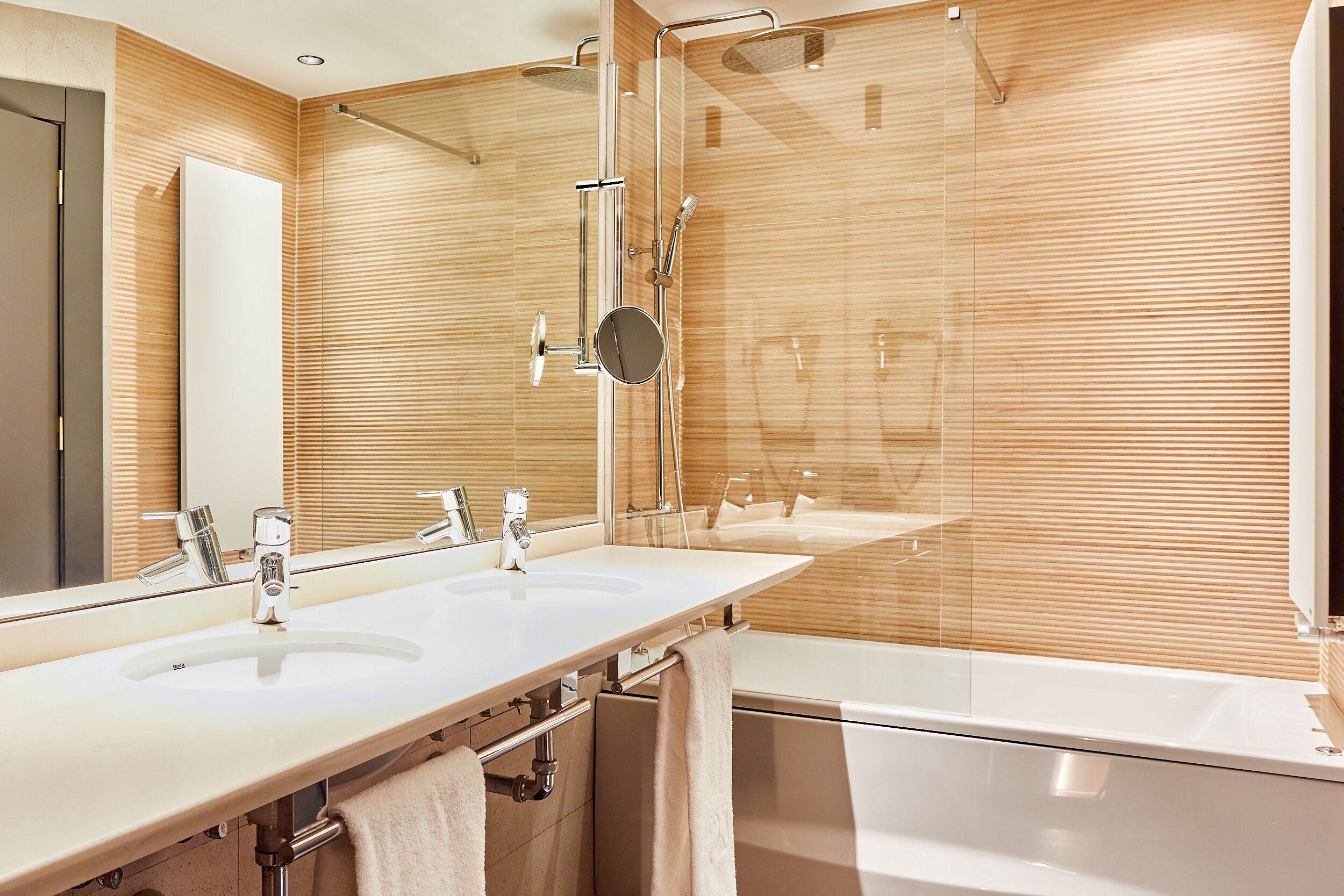 Un bagno moderno con due lavabi, uno specchio grande e una cabina doccia in vetro.