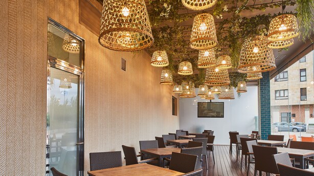 An outdoor dining area with wicker chairs and tables, hanging wicker lamps, and a view of the street.