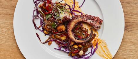 A white plate with octopus and vegetables on a wooden table.