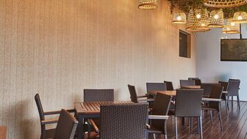 A restaurant with wicker chairs and tables, hanging wicker lamps, and a wall with a herringbone pattern.