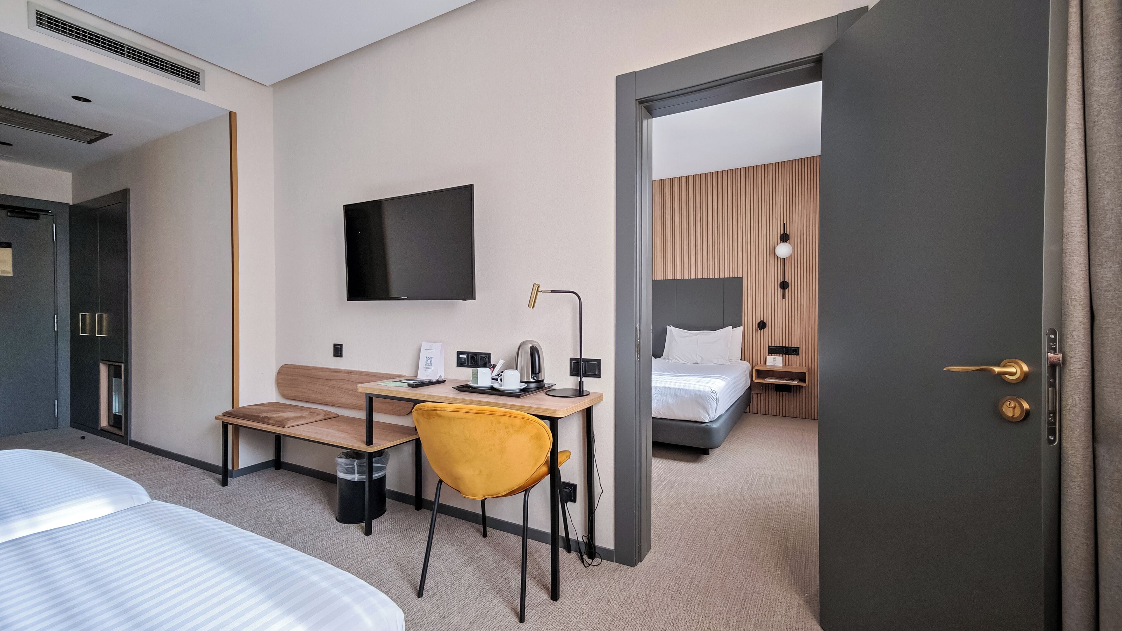 Una habitación de hotel con cama, escritorio con silla, televisión y mesita de noche con lámpara.