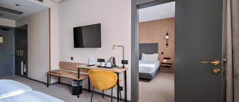 Una habitación de hotel con cama, escritorio con silla, televisión y mesita de noche con lámpara.