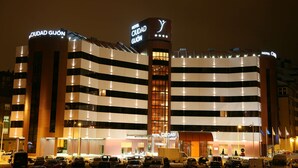 A hotel with multiple floors, a prominent sign reading "HOTEL CIUDAD GIJÓN," and a parking lot with several cars.