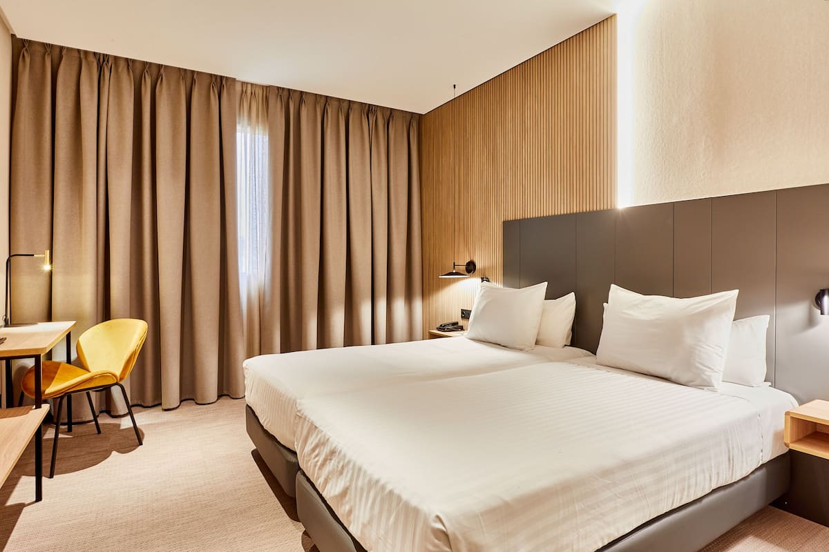 Ein Hotelzimmer mit einem großen Bett, einem Schreibtisch mit Stuhl und einem Fenster mit Vorhängen.