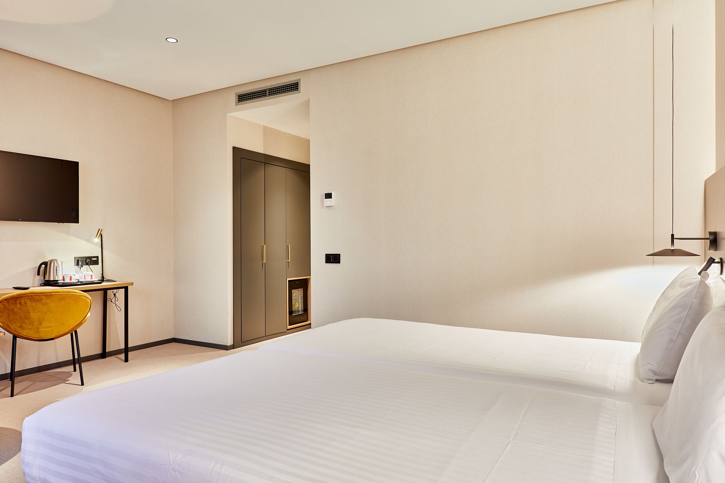 A hotel room with a large bed, a desk with a chair, a flat-screen TV, and a door leading to another room.