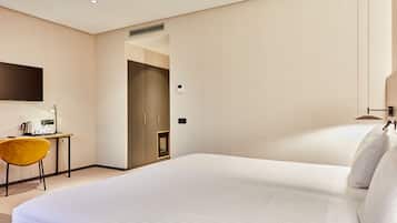 A hotel room with a large bed, a desk with a chair, a flat-screen TV, and a door leading to another room.