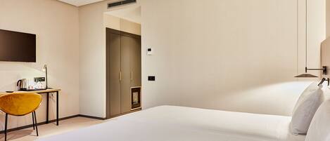 A hotel room with a large bed, a desk with a chair, a flat-screen TV, and a door leading to another room.