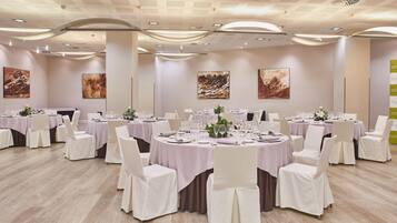 Un salón de banquetes con mesas redondas, sillas blancas y centros de mesa florales.