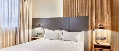 A hotel room with a large bed, wooden panel wall, bedside table with a lamp, and a phone.