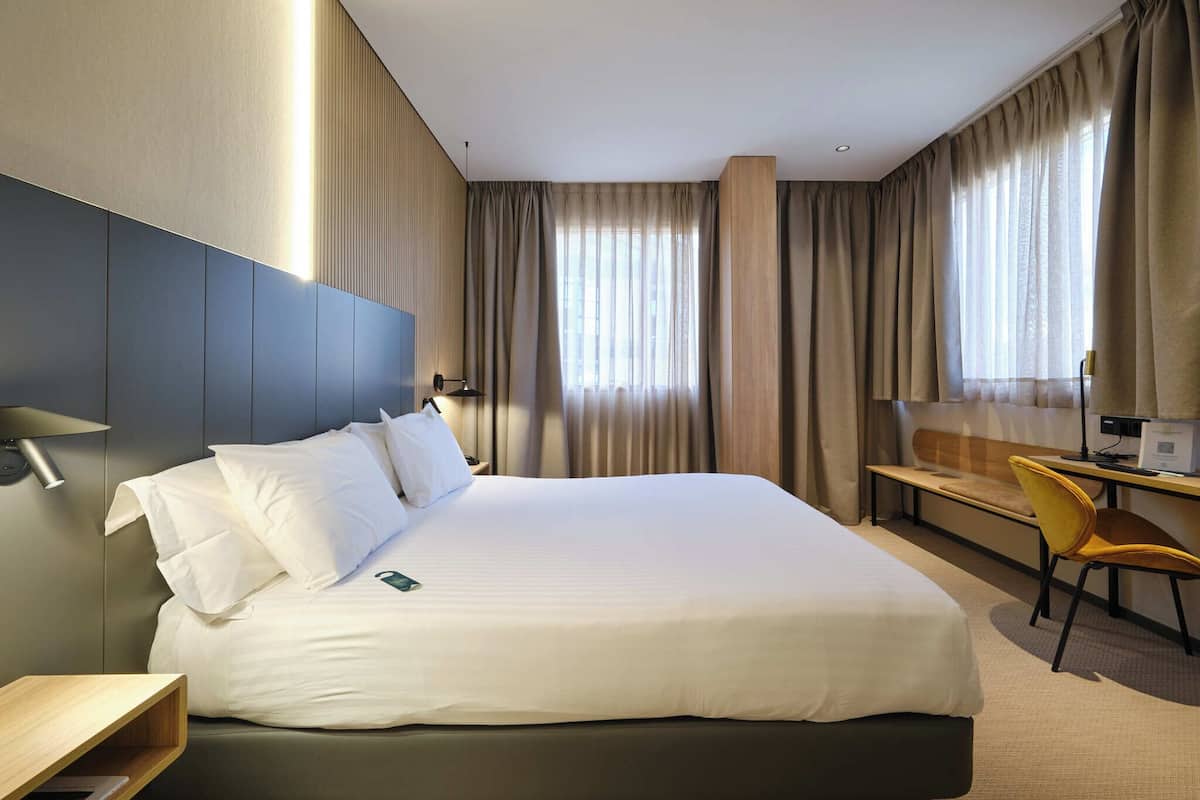 Ein Hotelzimmer mit einem großen Bett, einem Schreibtisch, einem Stuhl und einer Lampe.