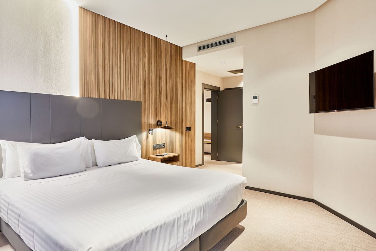 Ein modernes Hotelzimmer mit einem großen Bett, einer Wand mit Holzvertäfelung, einem Flachbildfernseher und einem Nachttisch mit Lampe.