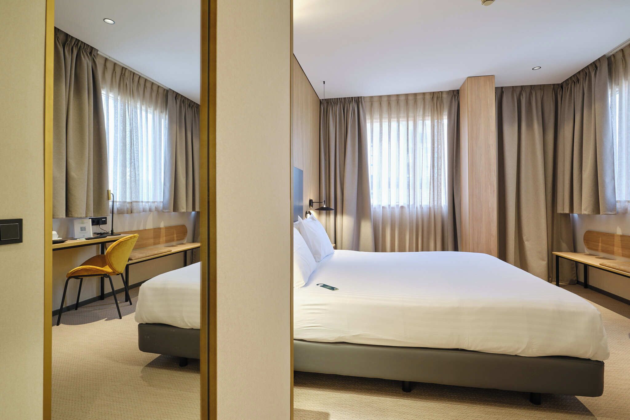 A hotel room with a bed, a desk with a chair, a TV, and curtains.