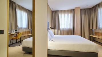 Una habitación de hotel con cama, escritorio, silla, televisor y cortinas.