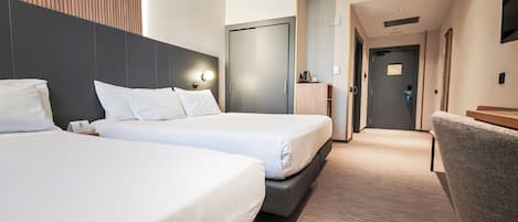 A hotel room with two beds, a desk, a chair, and a wardrobe.