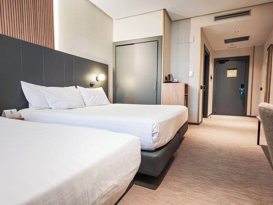 A hotel room with two beds, a desk, a chair, and a wardrobe.
