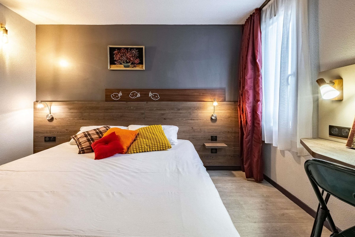 Quarto de hotel com uma cama grande, abajures, uma pequena mesa e um espelho.