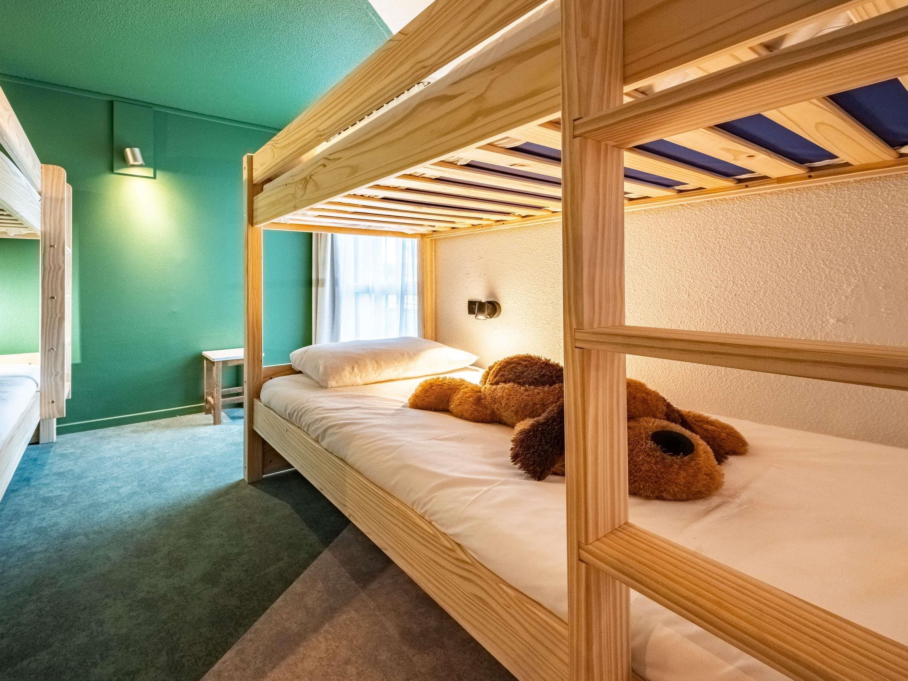 Ein Schlafzimmer mit Etagenbetten, einer grünen Wand, einem kleinen Tisch und einem Fenster.
