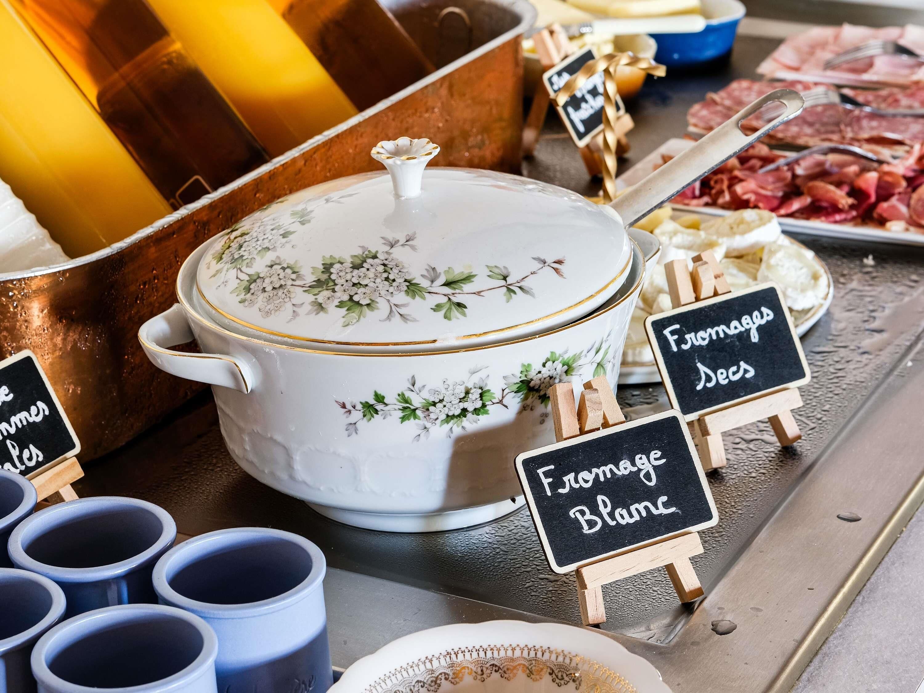 Un buffet avec un plat couvert, des plateaux de fromages et des panneaux indiquant les différents plats proposés.