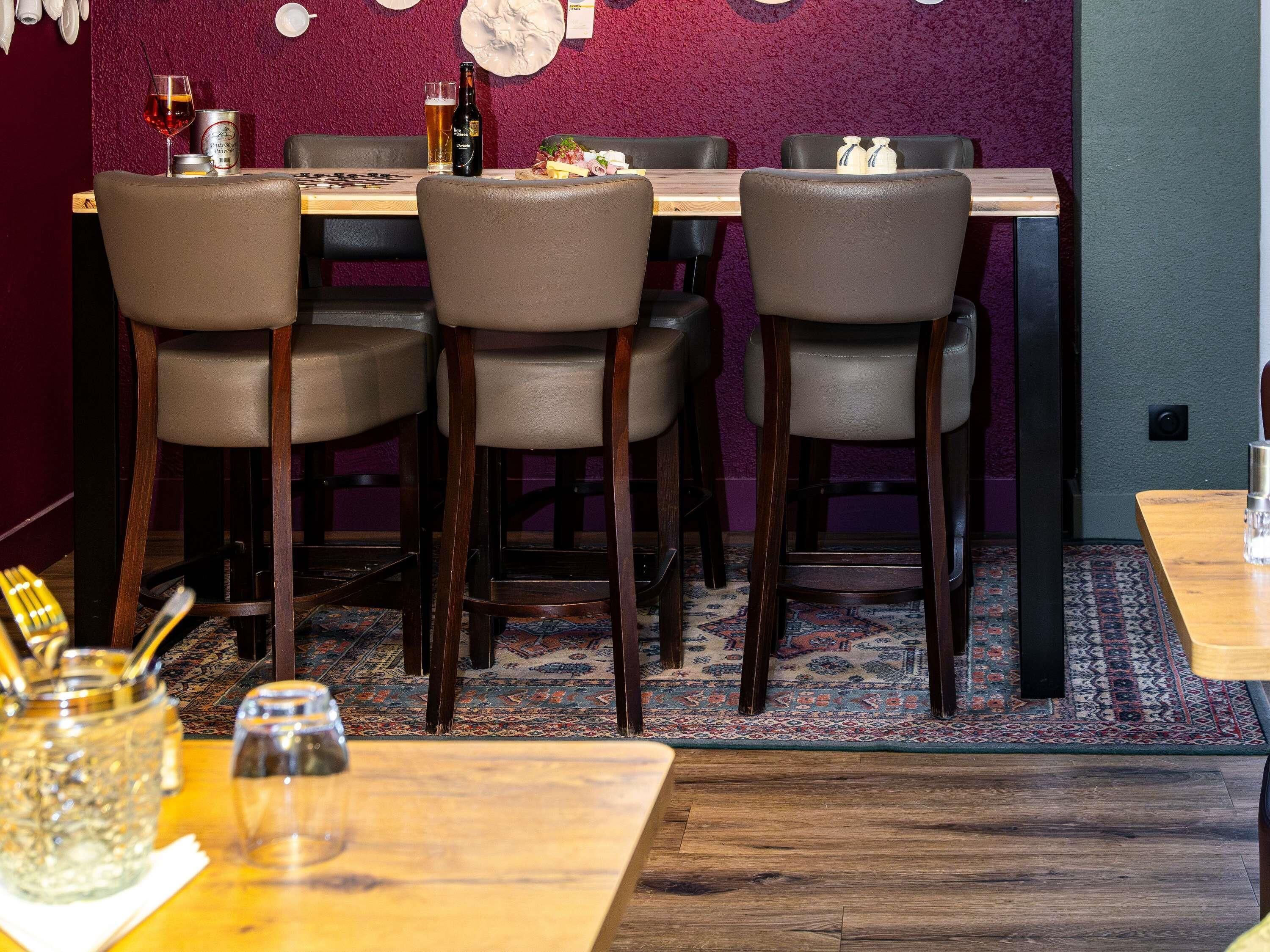 Interior de restaurante con una mesa de madera, cuatro sillas, piso alfombrado y una pared morada.