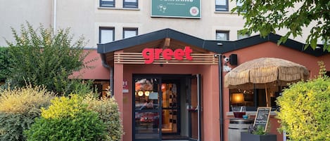 A building with a 'Greet' sign, a 'Maison Germains' sign, and a thatched umbrella outside.