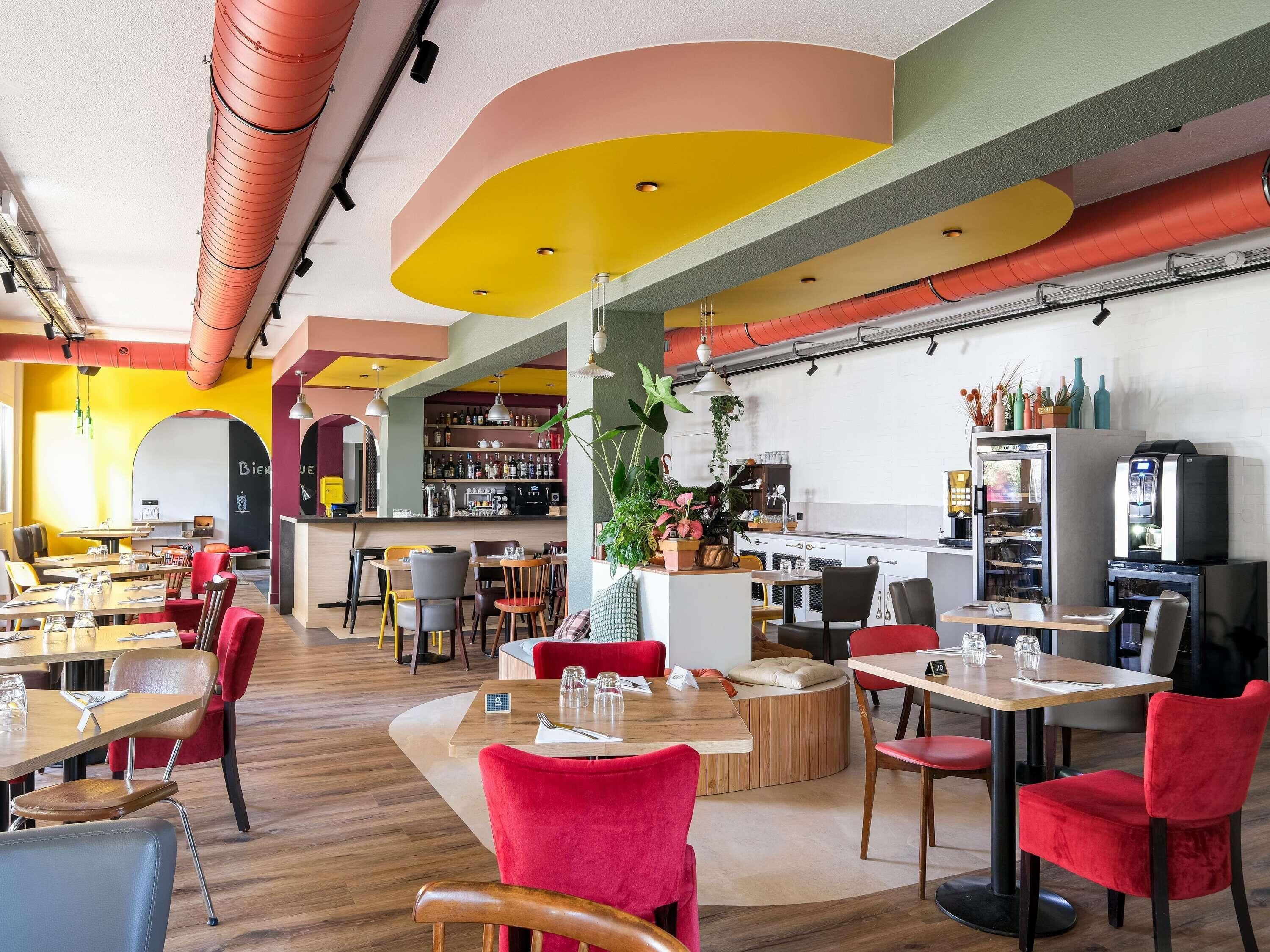 Interior de restaurante con varias mesas, sillas, una zona de bar y una variedad de plantas.