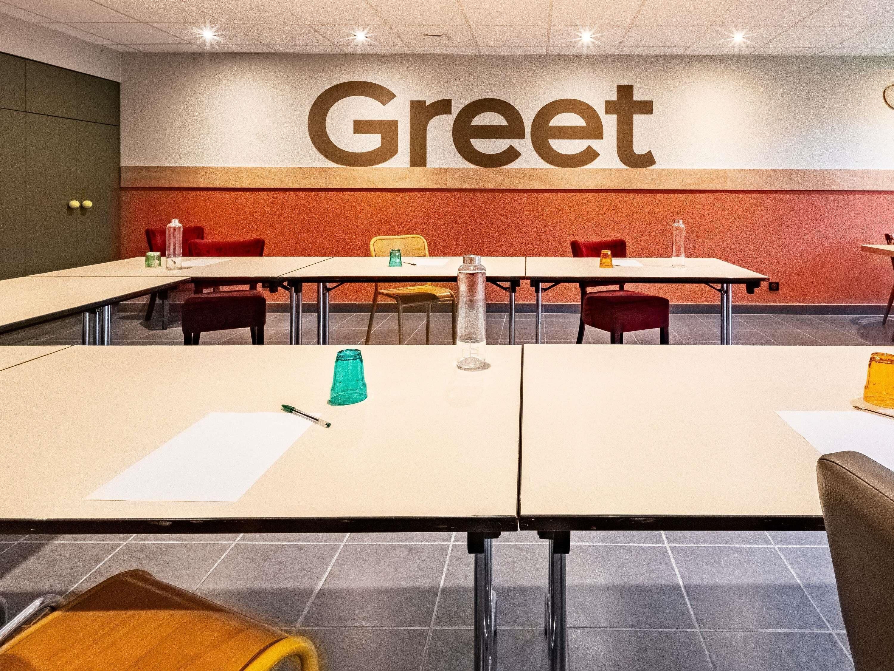 Une salle de conférence équipée de tables, de chaises et d’une pancarte « Bienvenue » au mur.