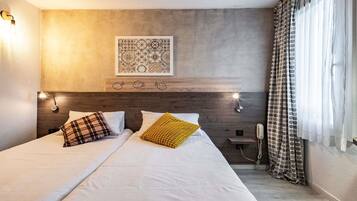 Habitación de hotel con cama, dos lámparas de noche, teléfono en la pared y ventana con cortinas.