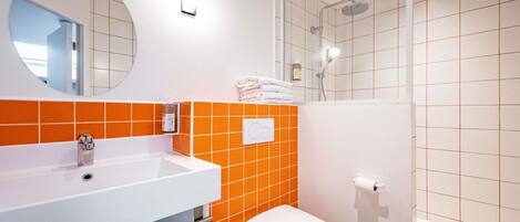 A bathroom with a white sink, orange-tiled walls, a toilet, and a shower.