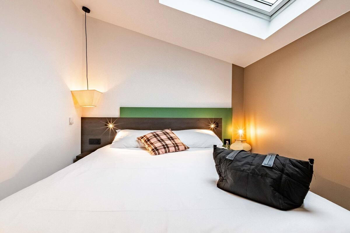 Une chambre d’hôtel avec un lit, un oreiller, une table de chevet, une lampe et une lucarne.