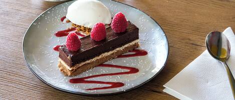 A dessert plate with a slice of cake, a scoop of ice cream, and raspberries on a table.