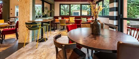 A modern dining area with a mix of wooden and metal furniture, large windows offering a view of the outdoors, and a variety of seating options.