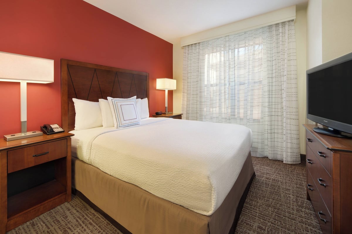 A hotel room with a large bed, two bedside tables with lamps, a television, and a window with curtains.