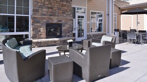 An outdoor patio area with wicker furniture, a stone fireplace, and a dining table with chairs. - Residence Inn by Marriott Loveland (Loveland)