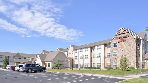 A multi-story hotel with a stone facade, multiple windows, and a parking lot with several cars. - Residence Inn by Marriott Loveland (Loveland)
