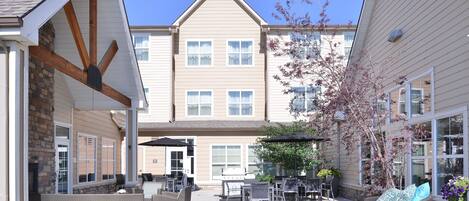 A patio area with outdoor furniture, a grill, and a view of a multi-story building.