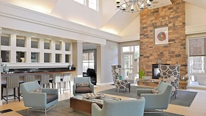 A spacious lobby with a high ceiling, a stone fireplace, and a bar area with multiple stools. - Residence Inn by Marriott Loveland (Loveland)