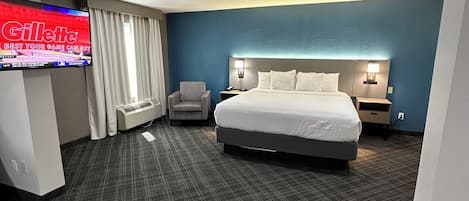 Quarto de hotel com uma cama grande, televisão de tela plana, escrivaninha e uma cadeira.