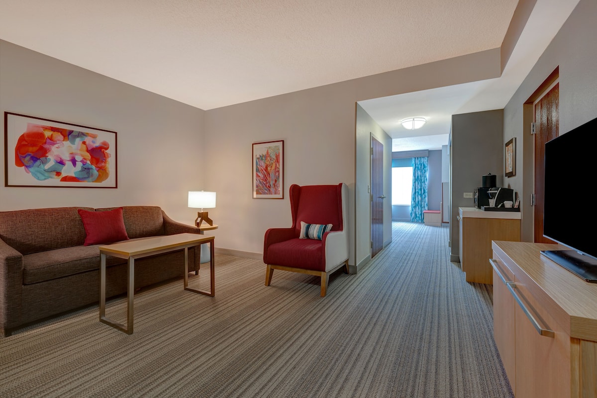 A hotel room with a sofa, armchair, small table, and a TV.