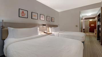 A hotel room with two beds, a bedside table with a lamp, and a wall with four framed pictures.