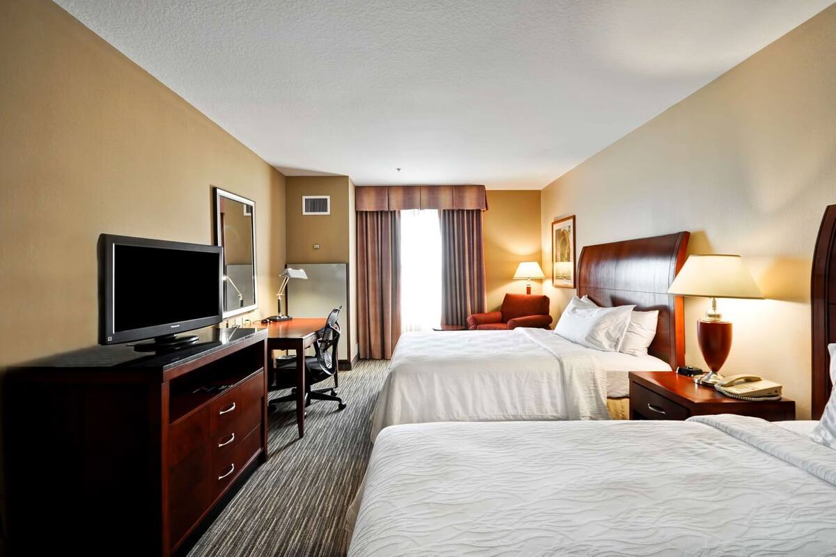 A hotel room with two beds, a desk with a TV, a chair, a lamp, and a nightstand with a phone.