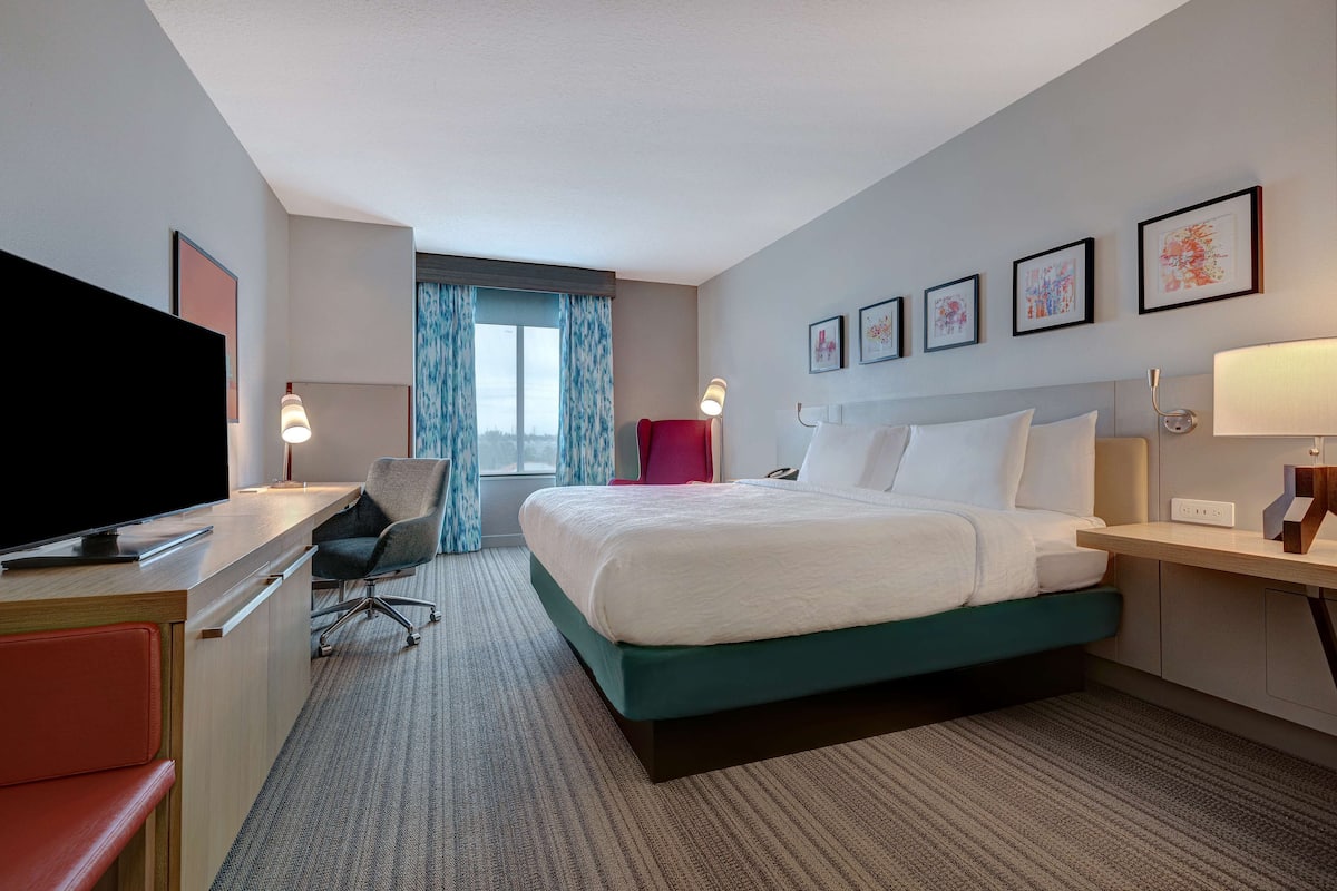 A hotel room with a bed, desk, chair, television, and artwork on the walls.