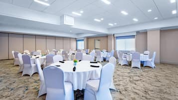 Un salón de conferencias con mesas redondas y sillas blancas, suelo alfombrado y un techo alto con iluminación empotrada.