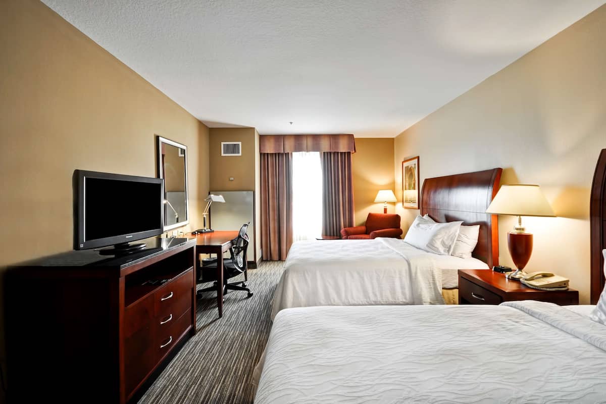 A hotel room with two beds, a desk with a television, a chair, a lamp, and a nightstand with a telephone.